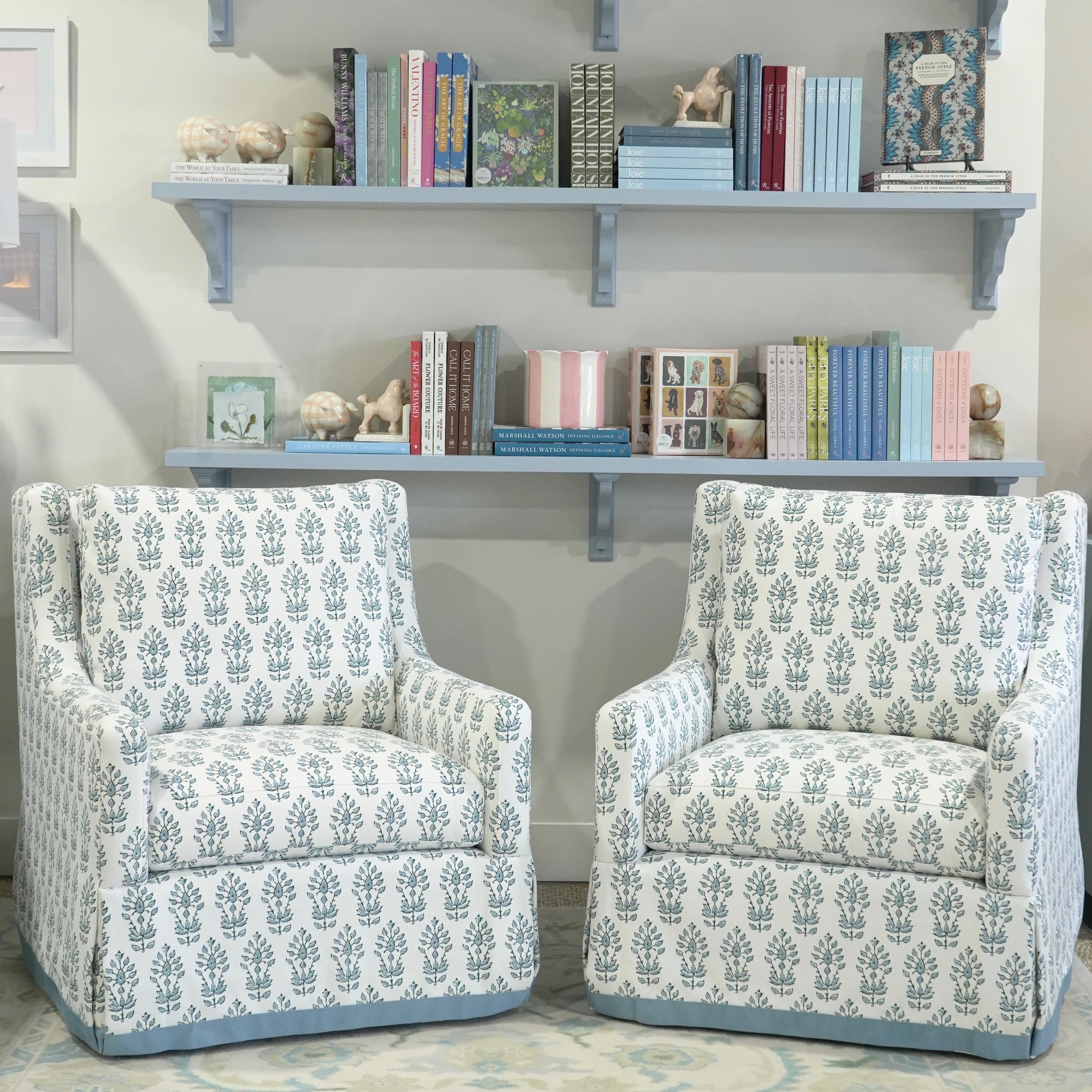 Two patterned armchairs in a room with a shelf displaying books and decorative items.