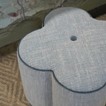 Gray floral-patterned ottoman on a patterned rug with a floral wallpaper background