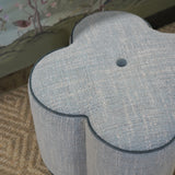 Gray floral-patterned ottoman on a patterned rug with a floral wallpaper background
