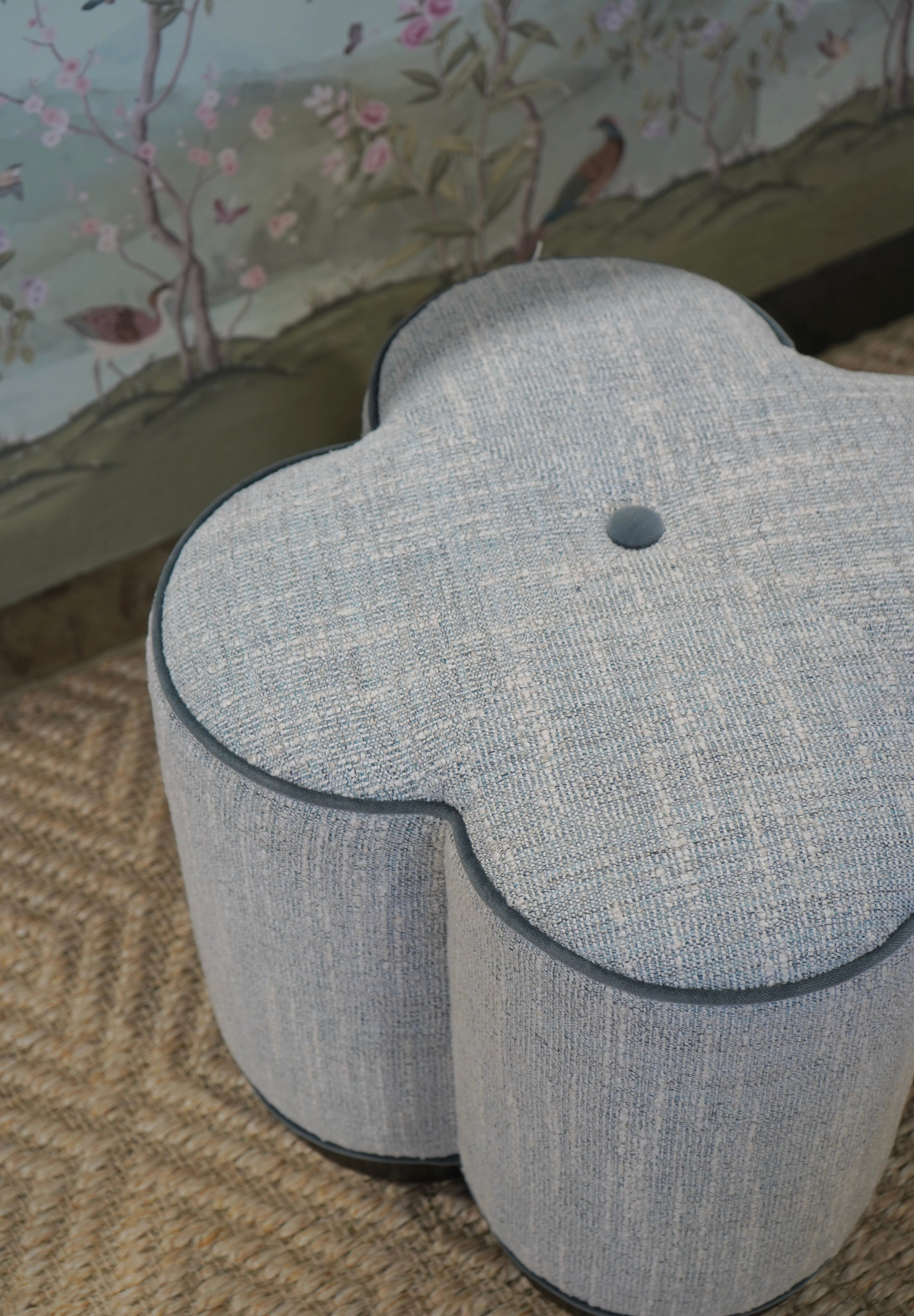 Gray floral-patterned ottoman on a patterned rug with a floral wallpaper background